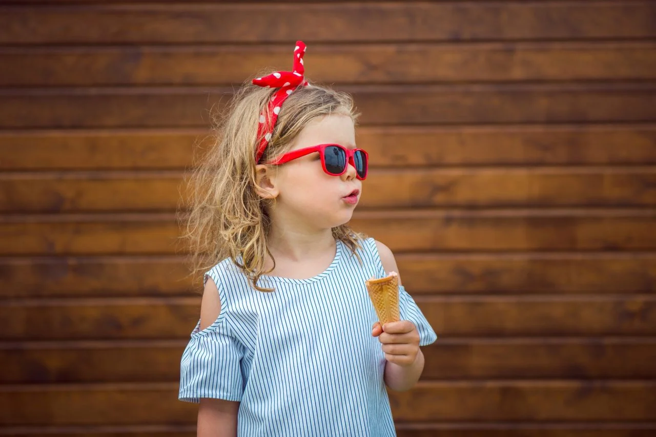 fashion-little-girl-wirh-bow-and-sunglasses-on-wooden-wall-background-eating-ice-cream