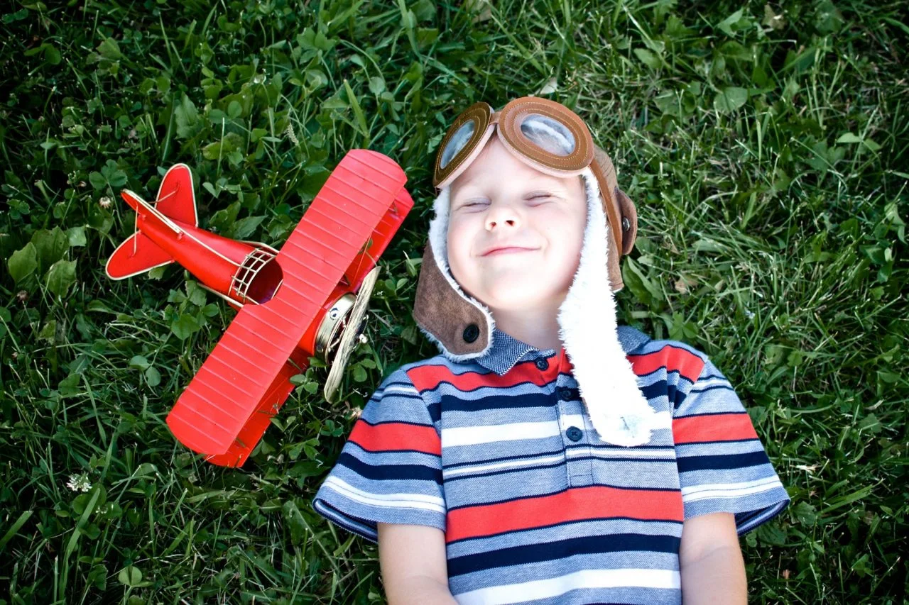 happy-child-lies-on-the-grass-next-to-a-red-toy-airplane